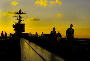 Back-lit by a golden sunset, Sailors walk toward the bow to muster for evening Foreign Object Damage (FOD) walkdown. (U.S. Navy photo by Photographer's Mate 3rd Class Lawrence M. Shannon) (Released)